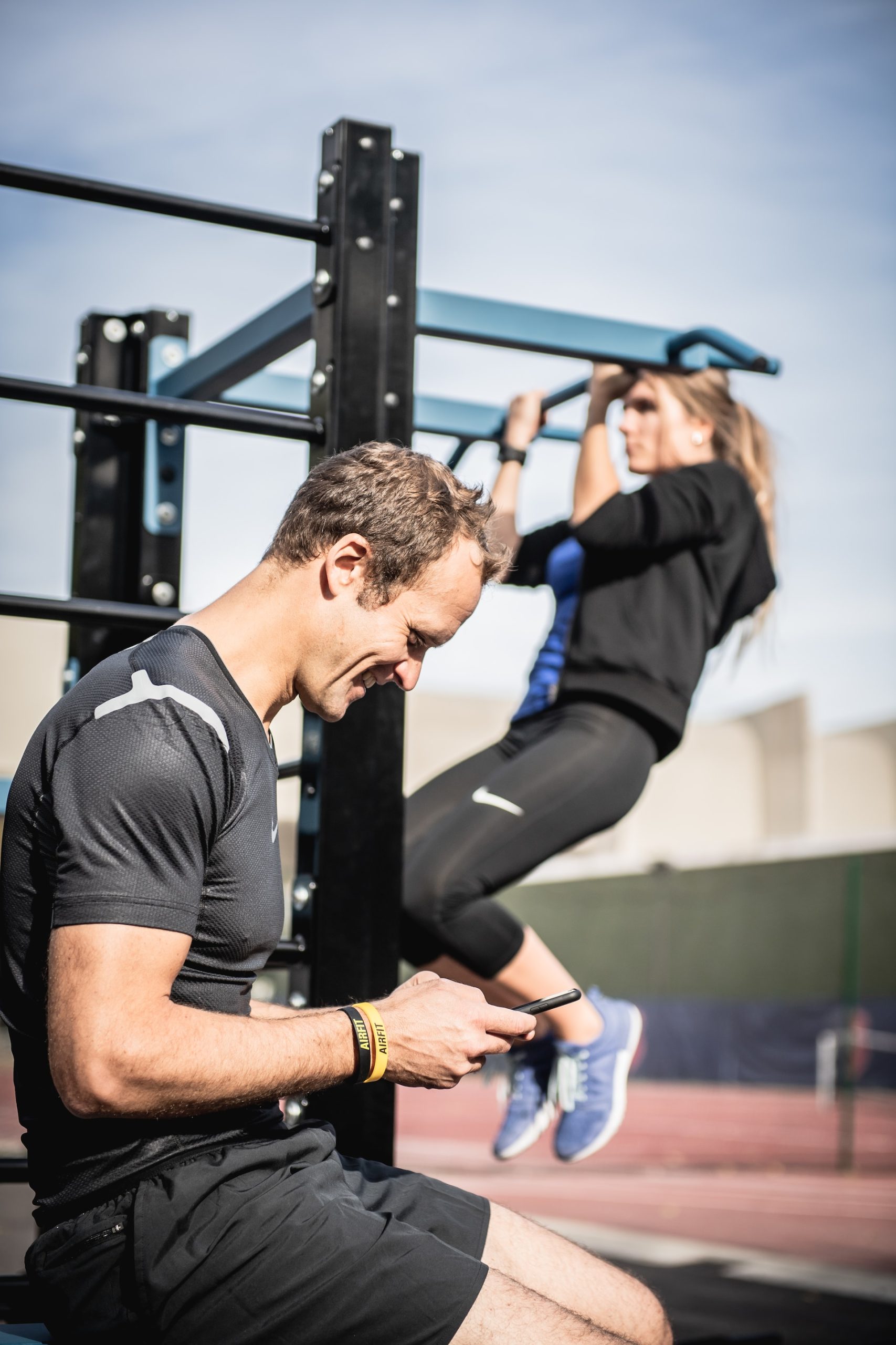 the image shows a man sitting on the phone and a woman pulling up on the horizontal bar