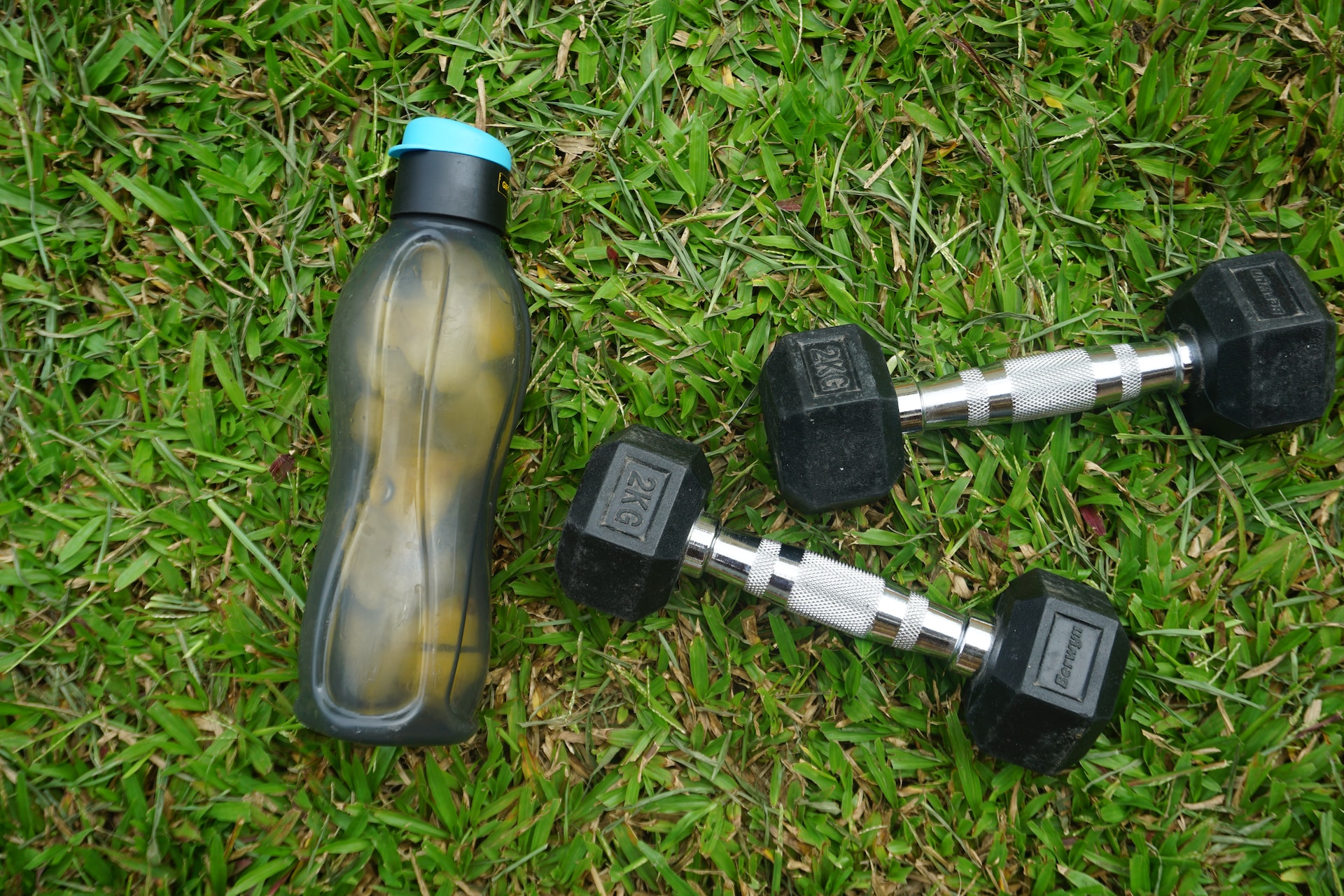 the image shows a bottle of water and dumbbells on the grass