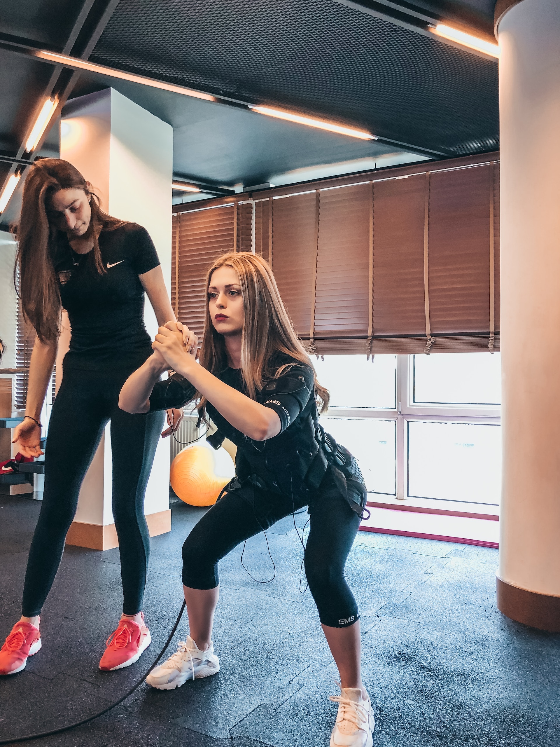 the image shows a woman doing squats with her trainer
